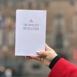 A hand holding up a copy of the book The Mindset Revolution