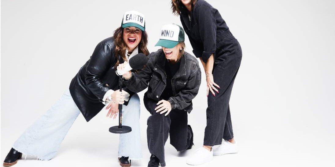 The three founders bent forward laughing in caps, studio backdrop