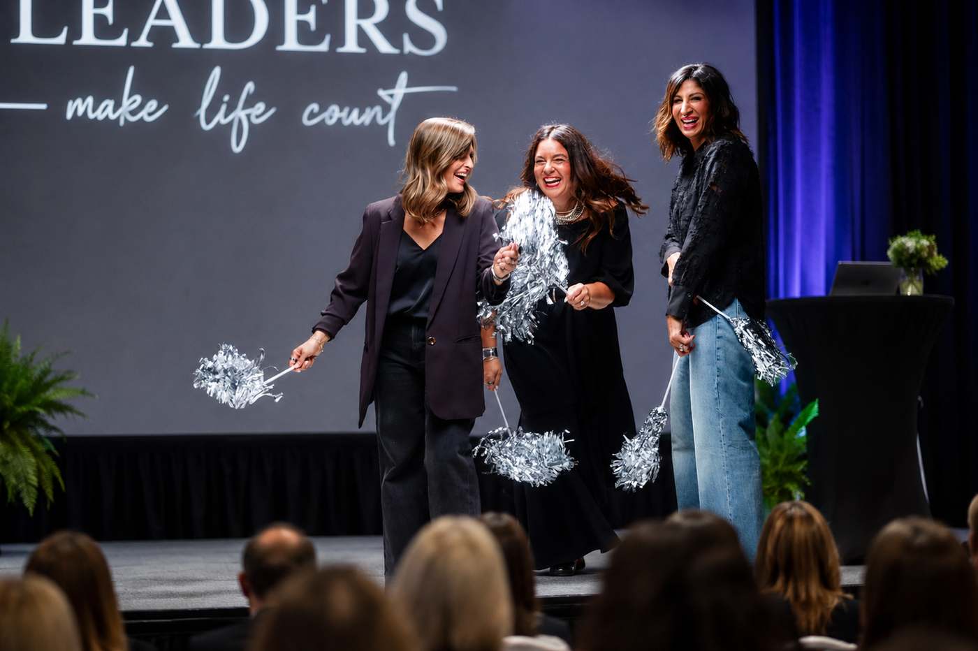 The Triad on stage at a conference with pom-poms, under a banner reading Leaders make life count